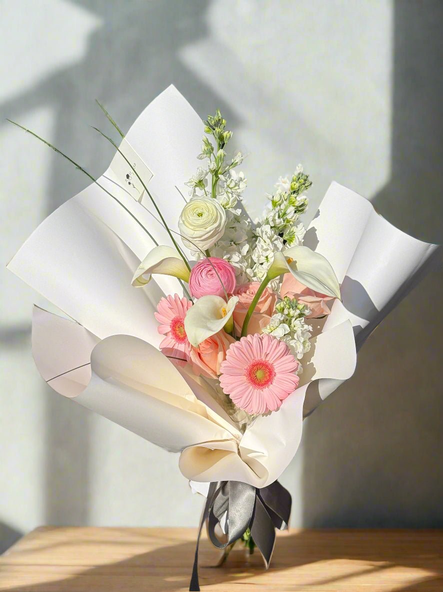 Everyday bouquet featuring soft pink and white seasonal flowers wrapped in clean white paper