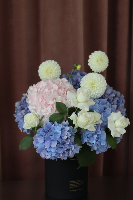 Pastel hydrangea flower arrangement in blue, pink and white with a soft rounded hug bucket design
