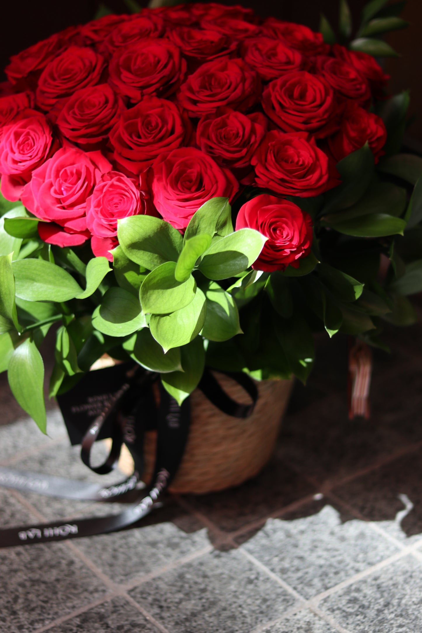 Close-up of luxury red roses arranged in a round rose basket with lush green foliage
