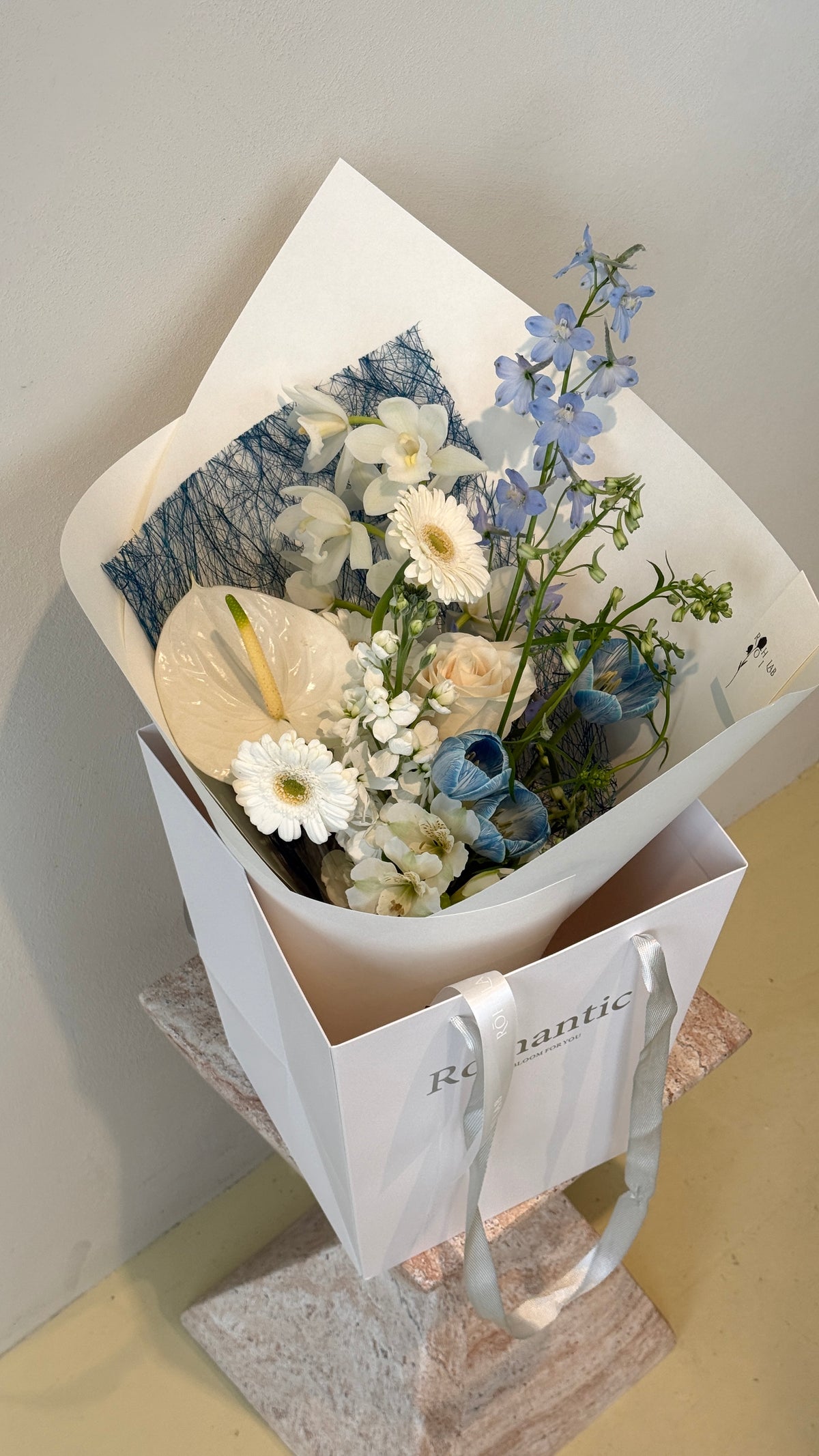 Blue and white seasonal flowers arranged in an elegant wrapped bouquet by Rōhi Lab