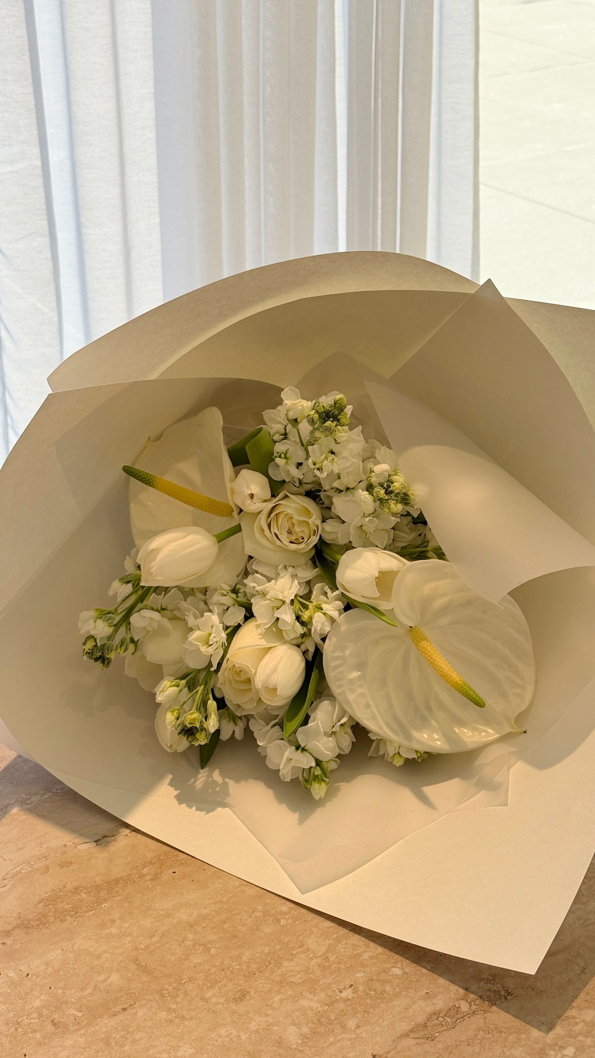 White seasonal flowers and lush green foliage arranged in a natural bouquet on a wooden table